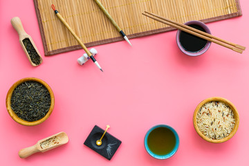 Chinese traditional symbols concept. Tea, rice, hieroglyph love, bamboo table mat, chopsticks, soy sause on pink background top view frame space for text