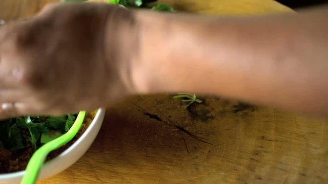 Asian chef cutting healthy green vegetables with knife on wooden chopping board and adding to bowl