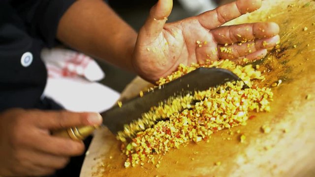 Asian chef preparing Basa gede chopping traditional spices on wooden cutting board in Balinese kitchen