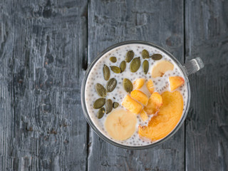 Chia seed pudding with banana and pumpkin seed and peach on a dark wooden table. The view from the top. Flat lay.