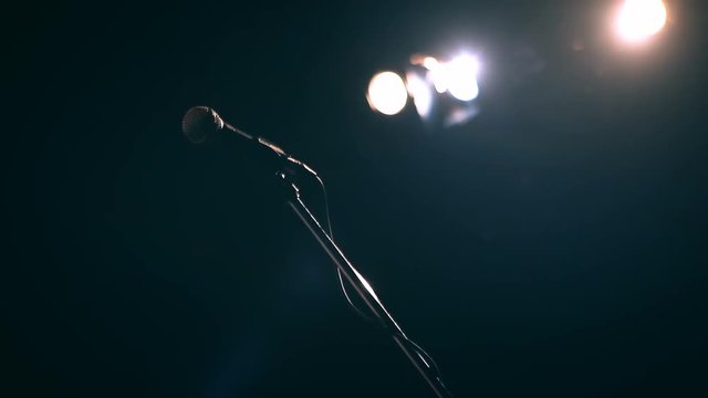 Beautiful slow motion shot of microphone on stand gleaming in stage lights at a live performance