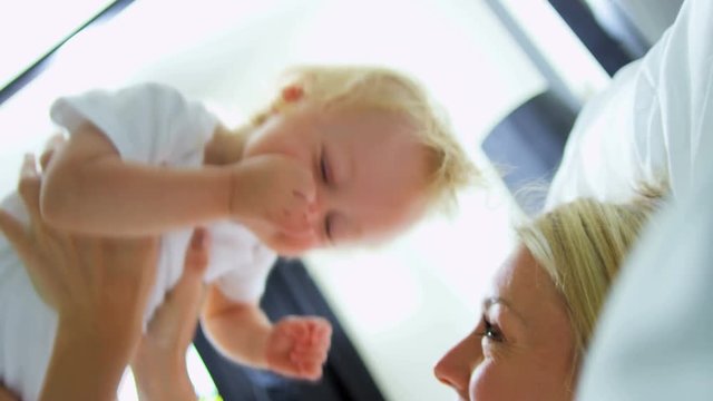 Cute young blonde Caucasian mother bouncing her young baby boy in her arms indoor 