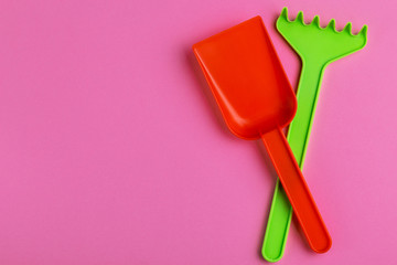 Colorful toy spade and rake on bright pink background
