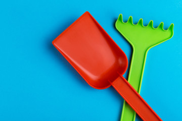 Colorful toy spade and rake on bright blue background