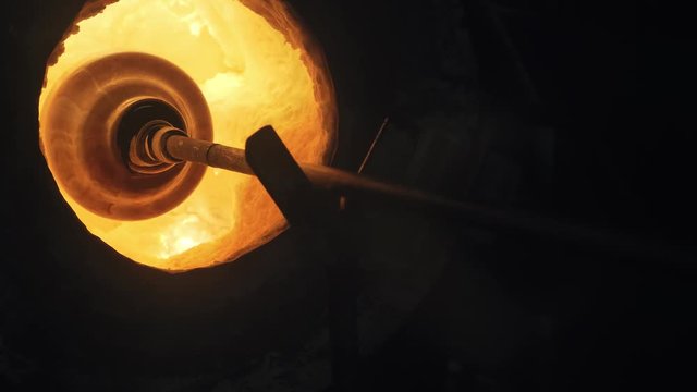 Glassblower heating a large glass bowl in the glory hole of the furnace