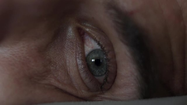 Macro close up of a man's eye opening, looking around, and looking at his phone.