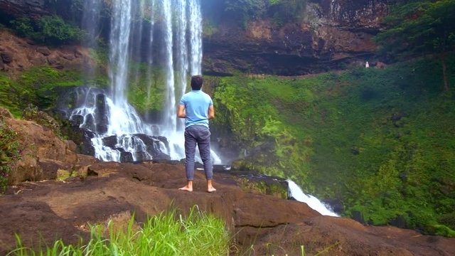 strong guy climbs up rock raises hands to greet waterfall