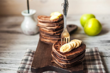 Heart-shaped chocolate pancakes on a red plate on a dark background. Pancake with banana, jam, apple, forks. Breakfast for your beloved on Valentine's Day