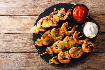 Fresh kebabs made from shrimps and pineapple slices decorated with green onions served with sauces...