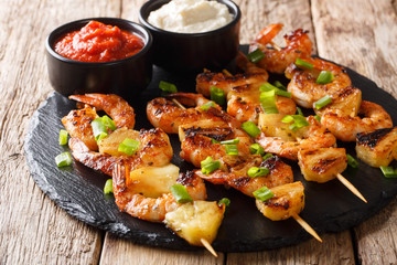 Delicious appetizer of kebab grilled shrimp and pineapple slices served with sauces close-up. horizontal