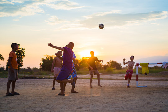 An action picture of a group of kid playing soccer football for exercise in community rural area under the sunset.