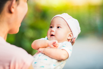 3 months baby feeling happy and smiles with her mother in the garden.Portrait of Asian family.