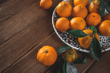 Fresh delicious mandarin oranges fruit or tangerines with green leaves in a bowl on wooden table