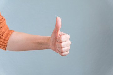 Female hand showing thumb up on blue background. Satisfaction concept.