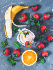 banana, strawberry and orange smoothies with mint in a glass with a straw on the table, top view