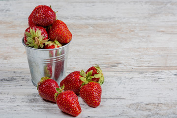 A bucket of fresh ripe strawberries, close-up on a light wooden background, copy space.