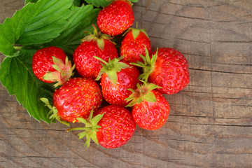 Bright ripe strawberries lying on a wooden table with green leaves. Close up view from top. with empty place for text.