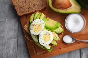 one avocado and sandwiches with egg and spices on a wooden Board