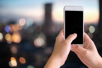 Smartphone on hands and empty device display on blur background city scape.