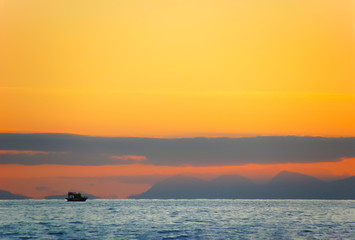 Sunset on the coast with clouds and a small pleasure craft.