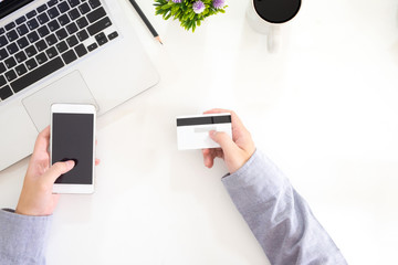 shopping online top view hands using smartphone and credit card with laptop computer on office desk buying in mobile technology.