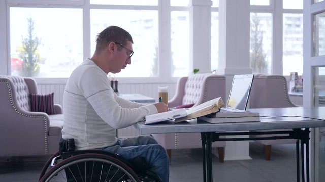 business freelance of disabled, successful ailing male on wheel chair uses modern computer technology for remote work to development of business ideas and making notes in notebook close-up sitting at