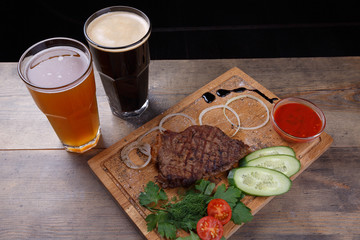 Steak with vegetable wedges and beer on a wooden cutting board