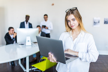 Successful business woman standing with laptop with her staff in background at modern bright office