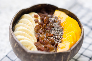 Oatmeal with banana, raisins, mango and chia seeds in coconut bowl