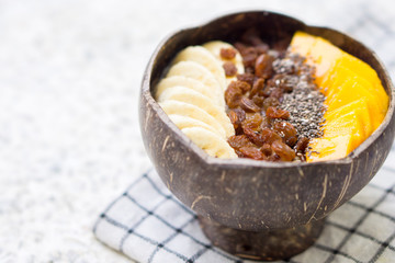 Oatmeal with banana, raisins, mango and chia seeds in coconut bowl
