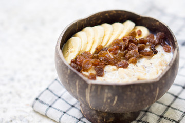 Oatmeal with banana, raisins and chia seeds in coconut bowl