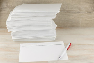 office work with correspondence: a Stack of blank envelopes on a wooden table, an envelope and a ballpoint pen lay ahead