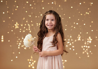 girl child is in christmas lights, yellow background, pink dress