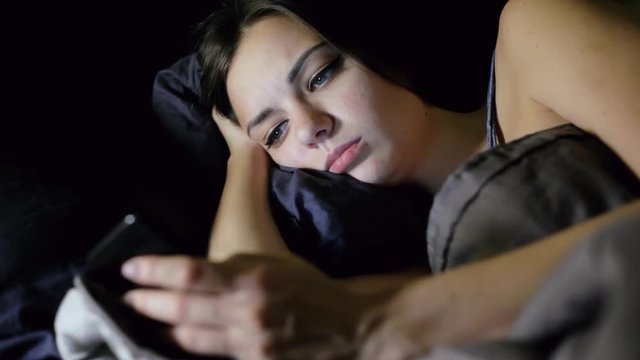 Woman surfing internet while lying in bed in the bedroom at night, looks photo, chating