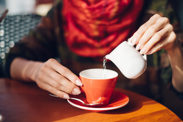 Woman’s hands pouring hot water in red coffee cup - woman sitting in cafe with soft drink
