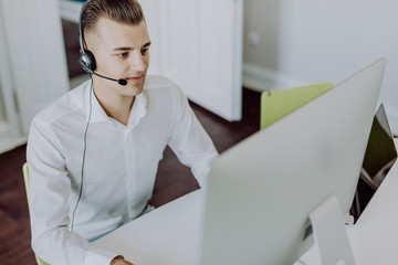 Portrait of a smiling young handsome man in formalwear with headset using computer in a office