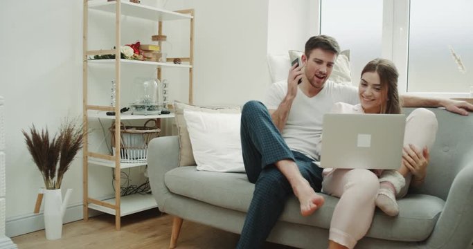 In the modern living room couple using a notebook order something and using a phone to make confirmation of order.