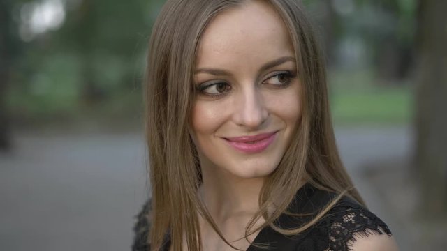Slow motion portrait of happy adorable smiling young woman posing in summer park. Smiling and looking into camera. Extreme close up.