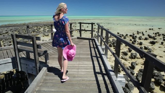 Woman in hat walking on wooden path at Stromatolites Hamelin Pool. Marine Reserve, Shark Bay, Western Australia. following girl in Australian travel destination.