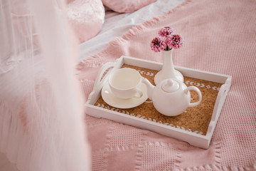 Breakfast in bed with flowers and white cups on tray.