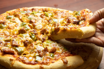 Pan Pizza slice take from hand side view with dark brown wood