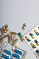 Tablets and capsules in a blister. Some started. Near scattered different pills. On a white background.