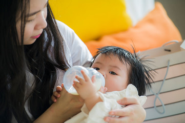 lifestyle candid portrait of young happy and sweet Asian Korean woman feeding her beautiful baby...