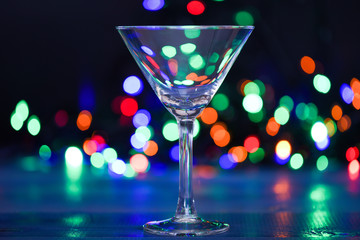 Cocktail glass on defocused garland colorful lights. What to drink on christmas party. Alcohol cocktail for winter party. Cocktail ideas concept. Easy recipes for winter alcoholic cocktail drinks