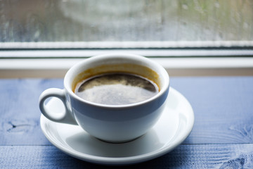Autumn cloudy weather better with caffeine drink. Enjoying coffee on rainy day. Fresh brewed coffee in white cup or mug on windowsill. Coffee time on rainy day. Wet glass window and cup of hot coffee