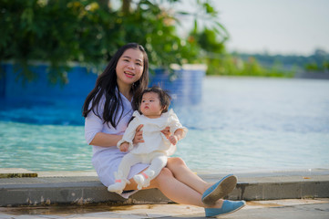 Fototapeta na wymiar young happy and cute Asian Korean woman playing with daughter baby girl at holidays tropical resort swimming pool enjoying summer holidays trip