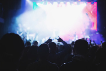 Silhouettes of a concert crowd in front of an illuminated stage in a nightclub.