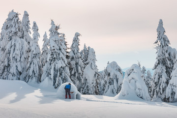 Man in blue jacket building igloo in the high mountain. Fantastic winter scene