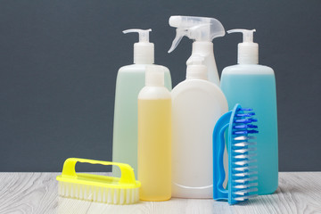 Bottles of detergent and brushes for cleaning on gray background.