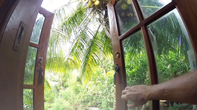 POV Camera moves towards into the palm trees garden window opened with male hand. Living in exotic nature concept video.
